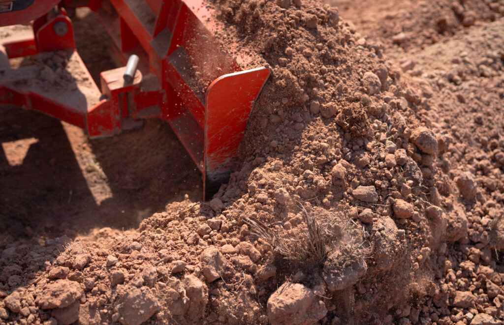 construction tractor with specialized dozer blade pushing and grading soil at excavation site. heavy machinery transforming raw land into prepared foundation for upcoming building development project.