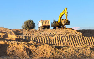 excavator loader with rised backhoe and a truck in a sky background