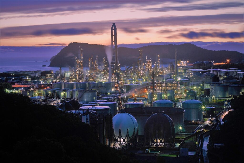 Large industrial refinery complex illuminated at dusk with storage tanks and processing towers near the Gulf Coast.